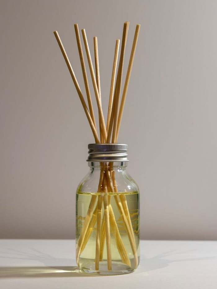 Minimalist reed diffuser in glass jar with aromatic liquid on gray background.