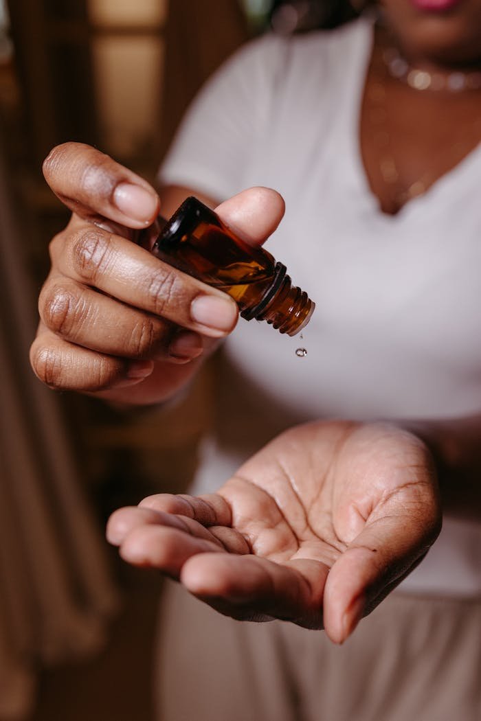 Close-up of a person pouring essential oil onto their palm from an amber vial.