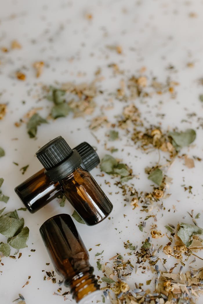 Close-up of amber essential oil bottles surrounded by dried herbs, evoking aromatherapy and natural healing.