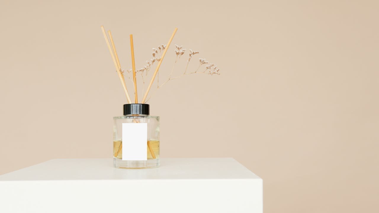 A minimalist reed diffuser with a mockup label on a white pedestal against a neutral background.