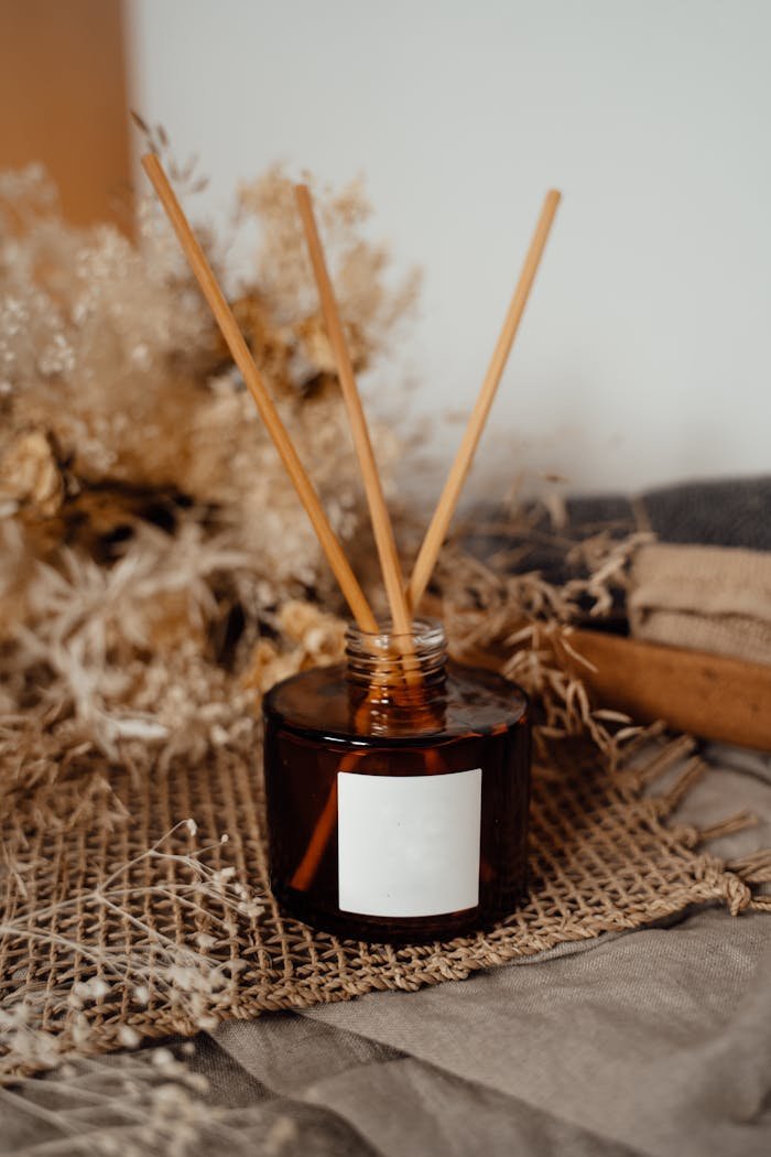 Aromatic reed diffuser bottle with reeds on a rustic burlap and dry floral background.