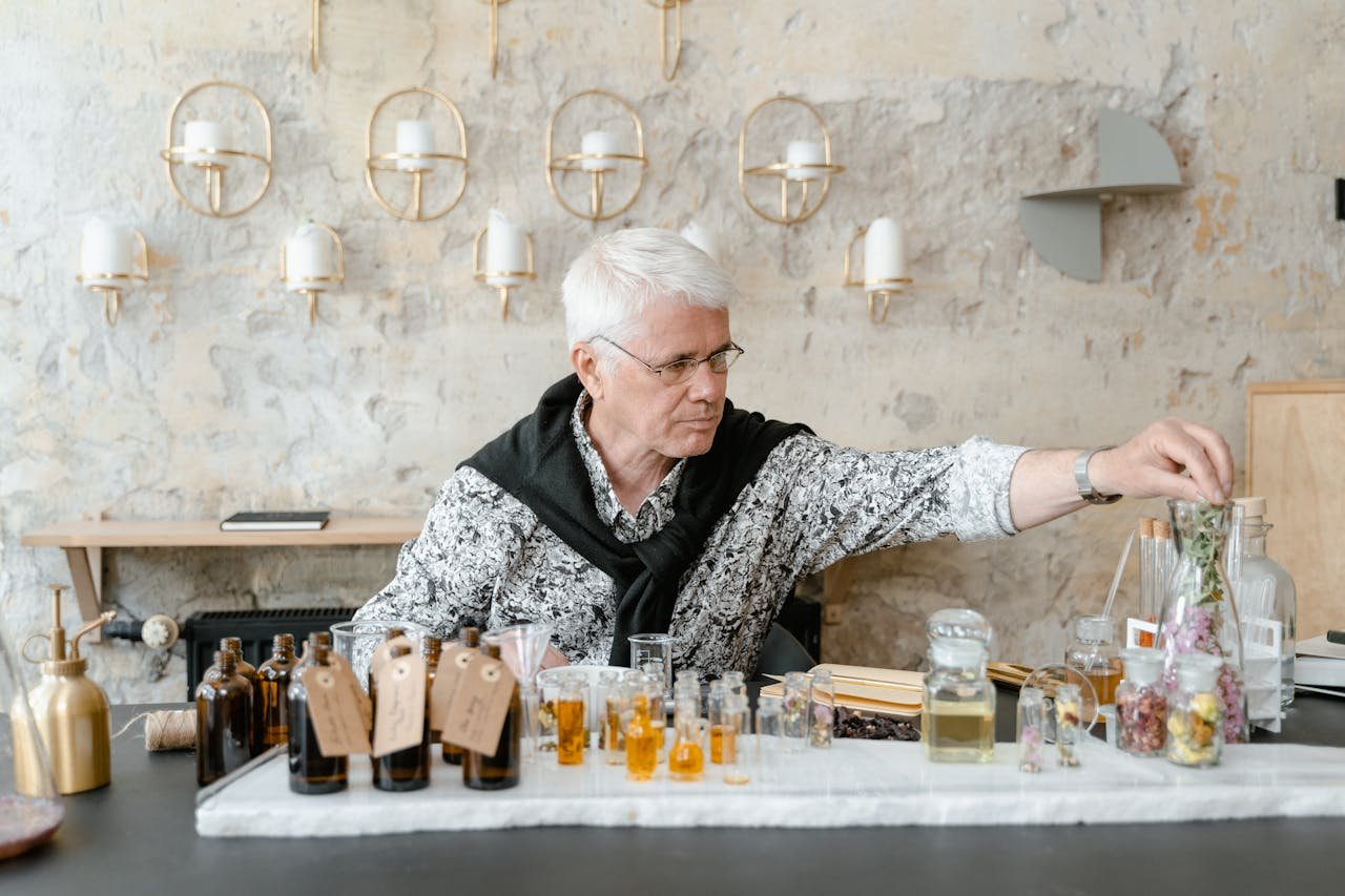 Senior man crafting scents in a perfumery workshop with glass bottles and natural ingredients.