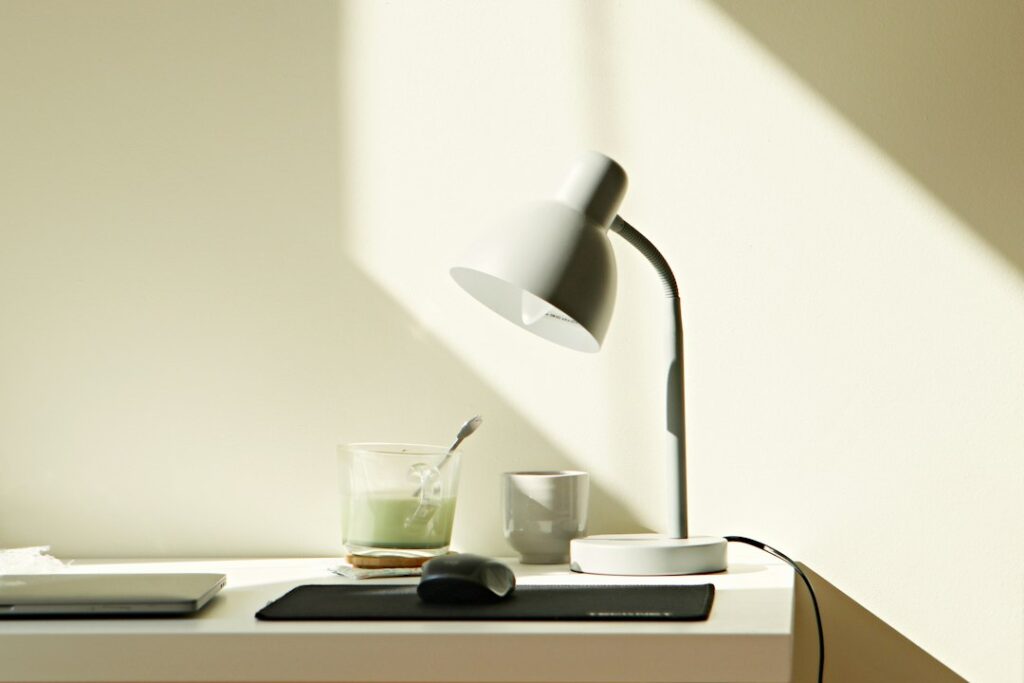 Tidy work desk with a laptop, lamp and cup of matcha tea in soft daylight